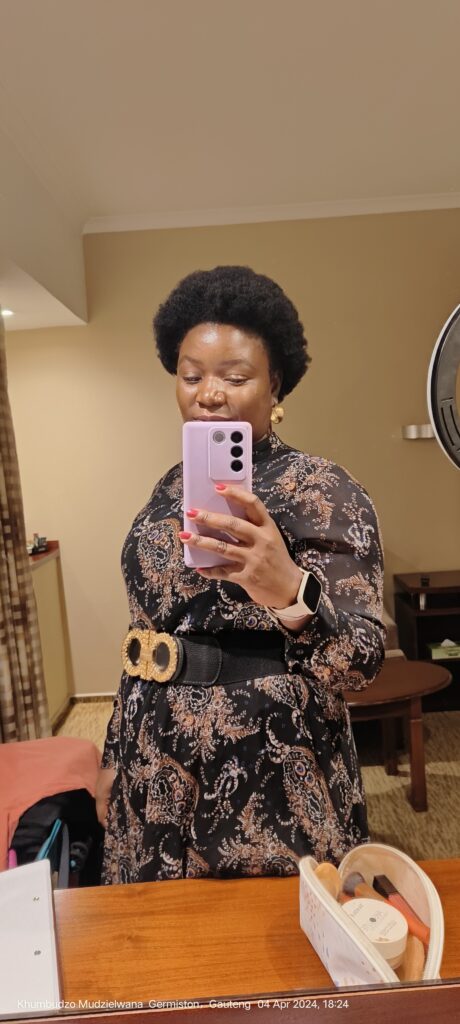 An african women with her afro wearing a black and brown dress holssing a purple phone taking a picture 
